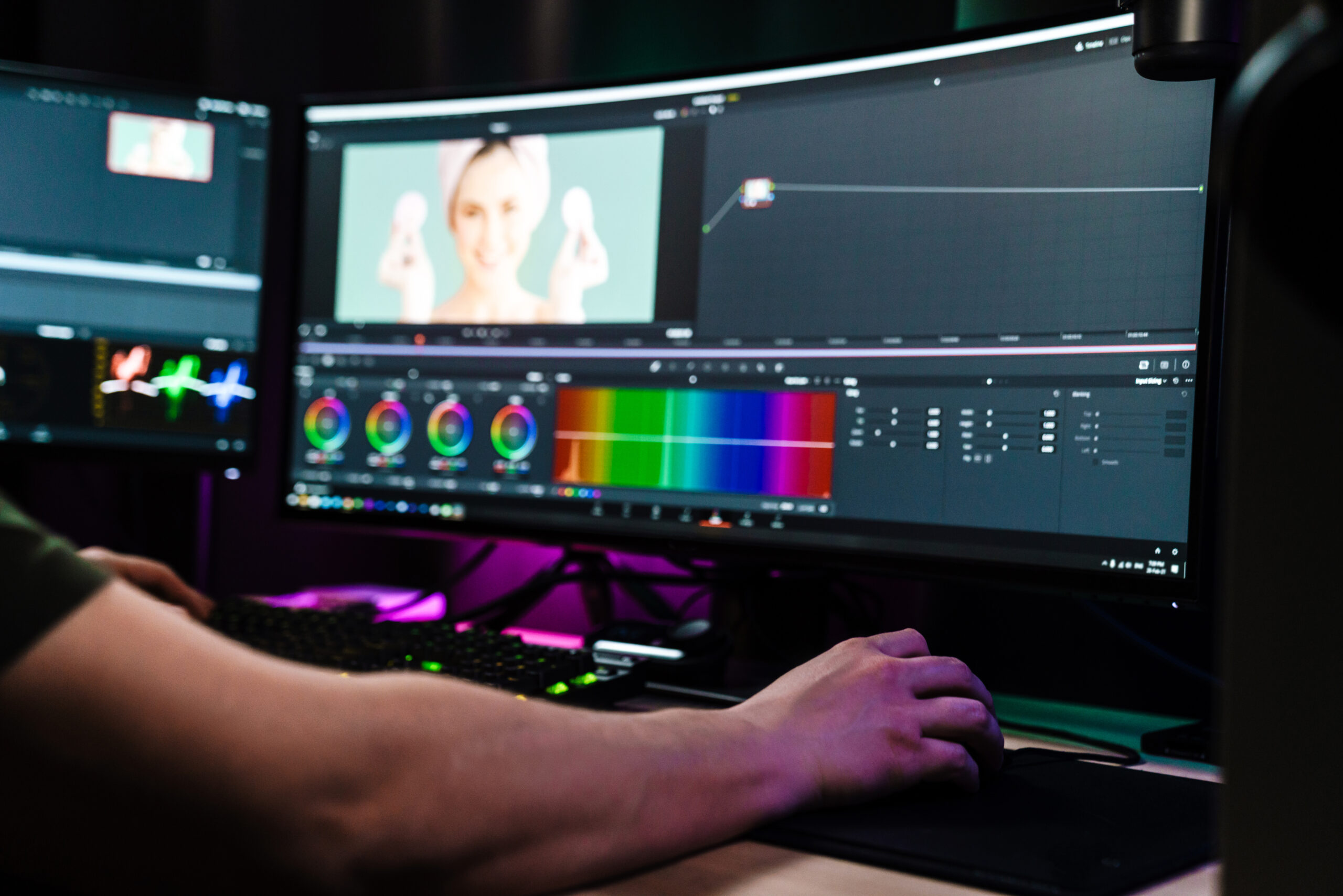 Back view of a young white man video editor sitting in front of a big screen working on a video montage indoors